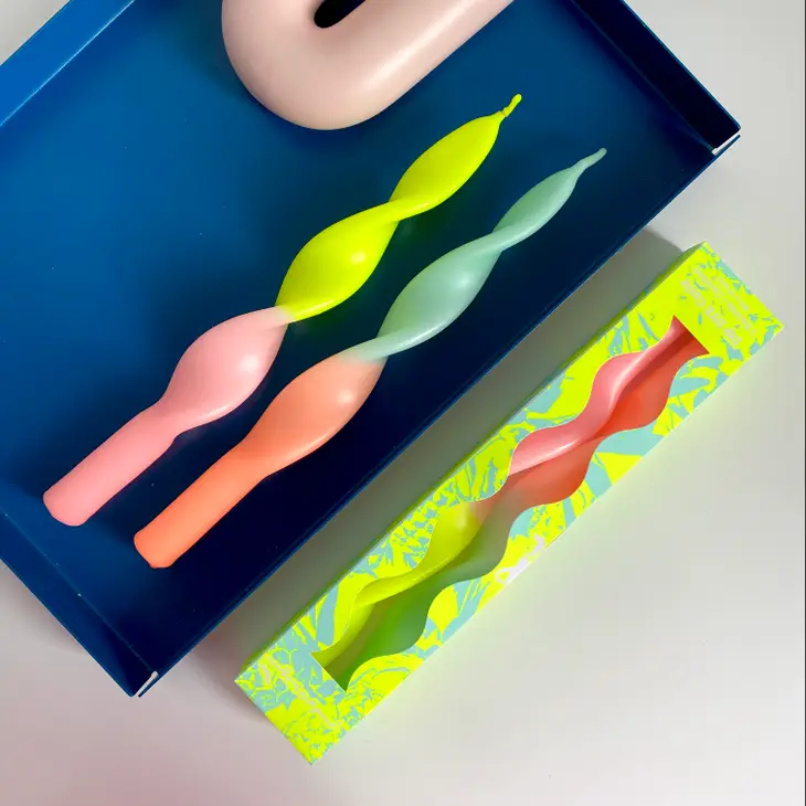 Velas torcidas coloridas em bandeja azul e caixa amarela com padrão verde