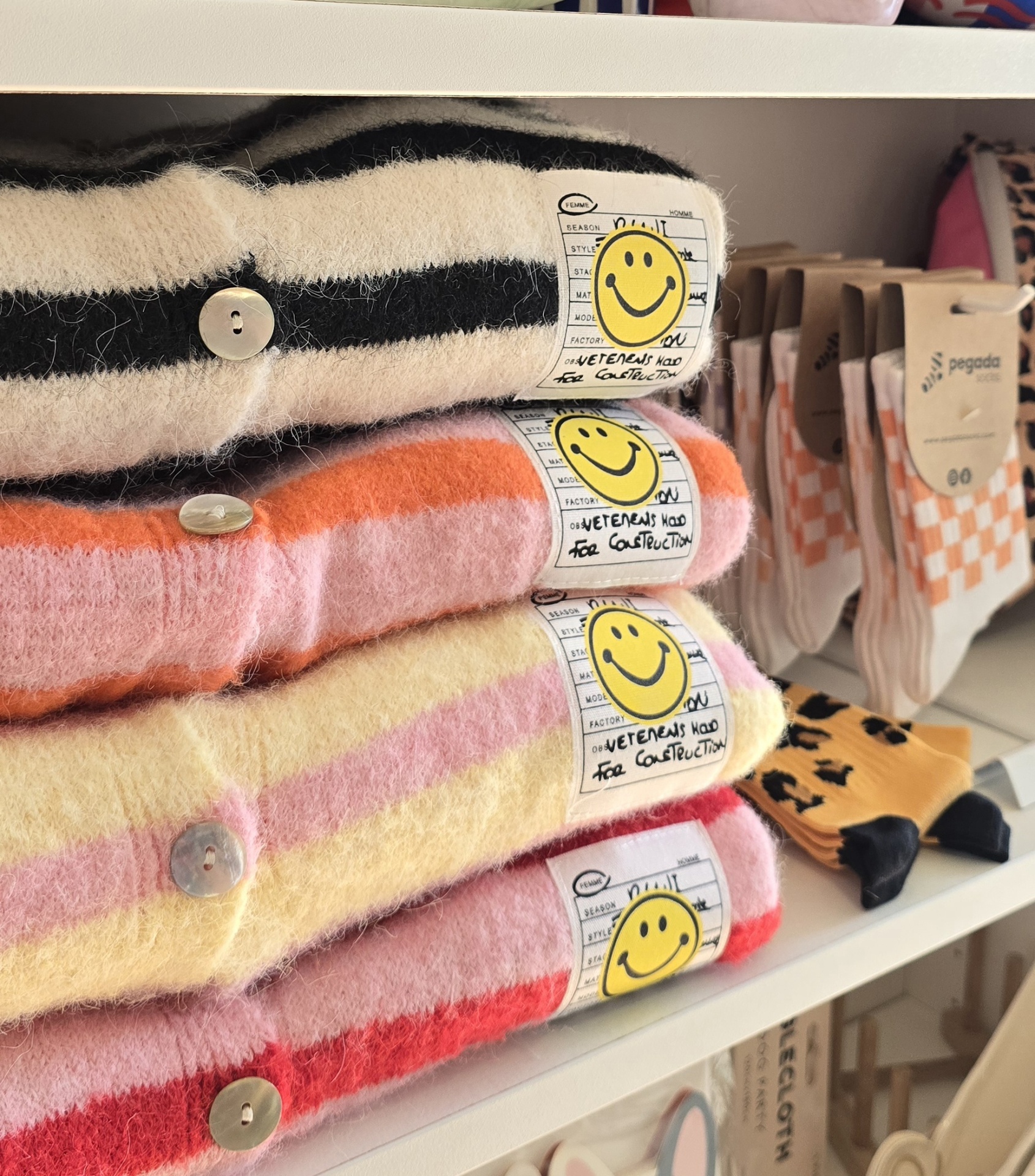 Camisolas listradas felpudas empilhadas com etiquetas amarelas sorridentes e meias coloridas ao lado
