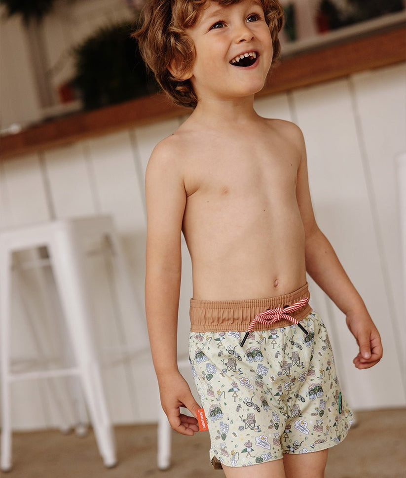 Calções de banho infantis com padrão colorido e cós castanho, criança de pé em ambiente interior