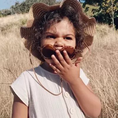 Criança com vestido branco, chapéu de palha e óculos de sol outdoors