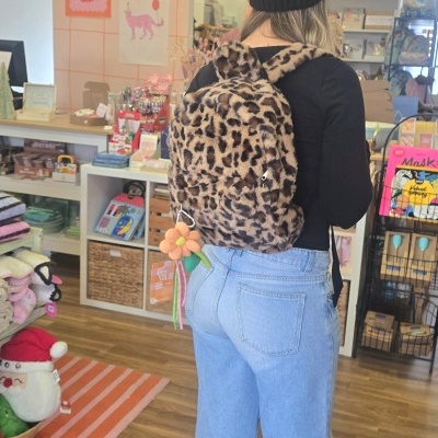 Mochila pelúcia padrão animal print usada por pessoa de costas numa loja