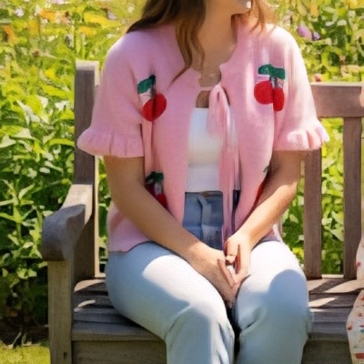 Mulher sentada num banco de madeira num jardim florido com camisola rosa decorada