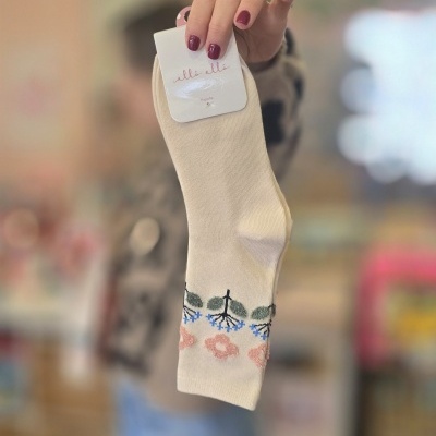 Meias creme com padrão floral e etiqueta da marca allò allò em fundo desfocado.