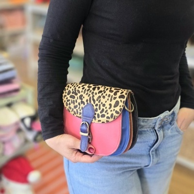 Bolsa pequena com padrão animal print e várias cores em corpo, segurada por pessoa com camisa preta e jeans claros.