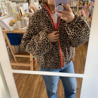 Casaco animal print com fecho laranja em pessoa a tirar selfie num espelho numa loja