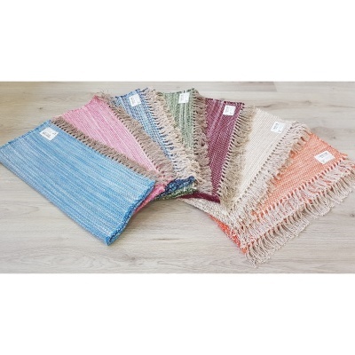 Tapetes coloridos trançados com franjas dispostos em leque sobre chão de madeira clara.