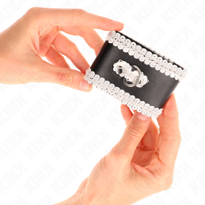 Pulseira larga preta com renda branca e detalhe metálico, segurada por mãos em fundo branco