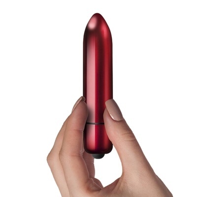 Vibrador metálico vermelho em formato de cápsula segurado por uma mão feminina