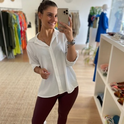 Mulher com camisa branca, calças vinho e sapatilhas brancas numa loja de roupa e acessórios