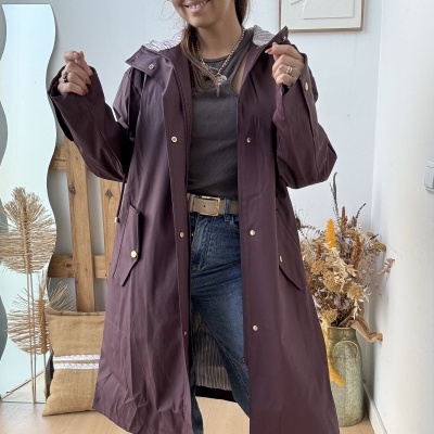 Casaco comprido castanho escuro com forro riscado e botões dourados num ambiente interior