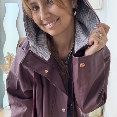 Capa impermeável vinho com capuz e interior às riscas usada por modelo sorridente