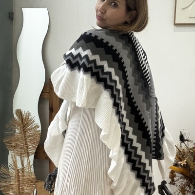Mulher de costas com vestido branco e poncho de padrão zigzag cinza, preto e branco com franjas