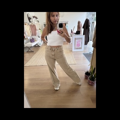 Mulher a tirar selfie num espelho, usando top branco e calças largas bege numa loja com decoração neutra.