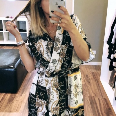 Vestido midi com padrão em branco, preto e dourado, manga curta, tecido leve, em ambiente interior com chão de madeira