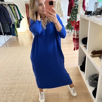 Mulher com vestido azul royal comprido de malha e sapatilhas brancas em loja de roupa com decoração natalícia