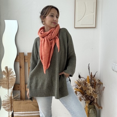 Mulher com camisola verde, cachecol laranja e botas pretas em ambiente interior decorado.