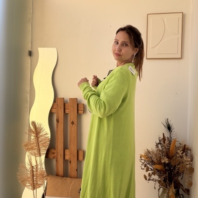 Mulher com vestido verde claro longo de malha num ambiente interior decorado.