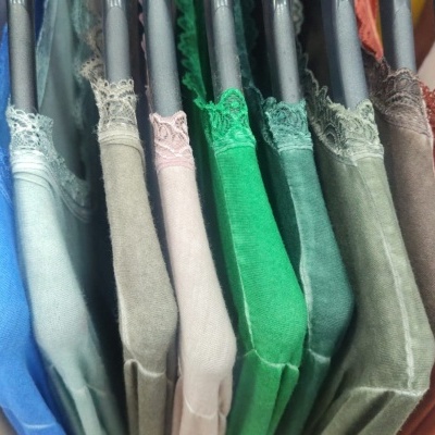 Camisolas coloridas com acabamento em renda penduradas em cabides de madeira