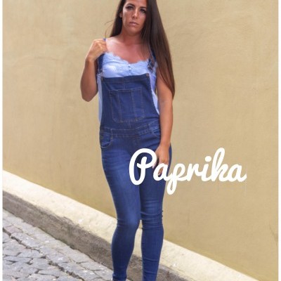 Macacão de ganga azul escura com bolso frontal em modelo feminino, parede amarela e chão de calçada portuguesa