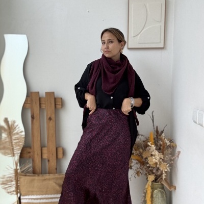 Mulher com roupa preta e vermelha vinho num espaço decorado com espelho ondulado, almofada e flores secas.