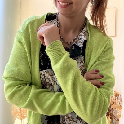 Mulher com cardigan verde claro e blusa decorativa num ambiente interior claro