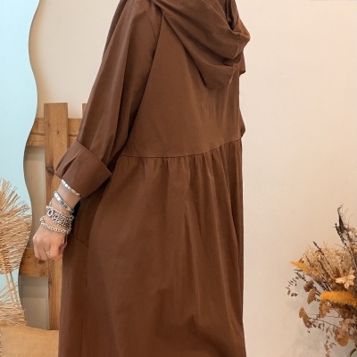 Vestido castanho comprido com capuz e mangas dobradas usado por mulher com pulseiras e óculos