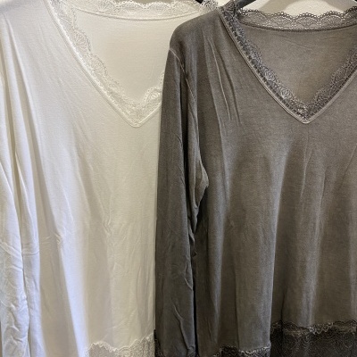 Duas blusas de manga comprida branca e cinza com renda nos decotes em V e nas barras, penduradas em cabides