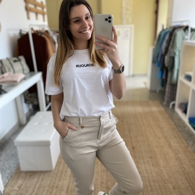 mulher a usar camisola branca com texto 'BONJOUR' e calças bege em loja de roupa