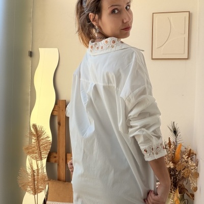 Mulher a usar blusa branca bordada com motivos florais laranja