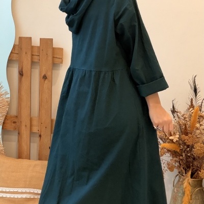 Vestido comprido verde escuro com capuz em ambiente interior