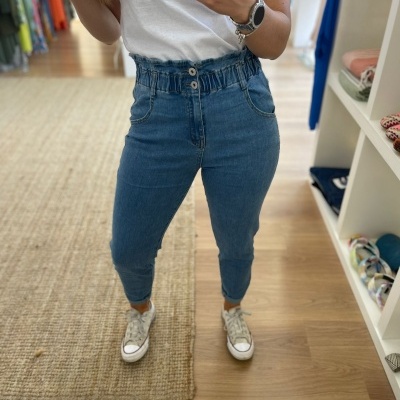 Calças de ganga azul com cintura elástica e botões, t-shirt branca e ténis brancos em loja