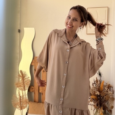 Vestido bege com botões e folho usado por mulher sorridente em ambiente interior decorado