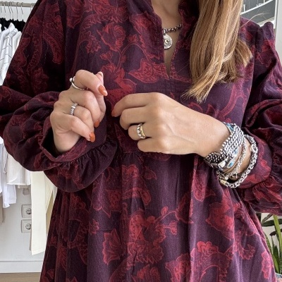 Vestido bordô com padrão floral usado por mulher com pulseiras e anéis