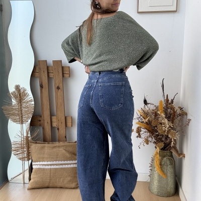 Mulher de costas com camisola verde e calças ganga azul escuro em ambiente interior com decoração