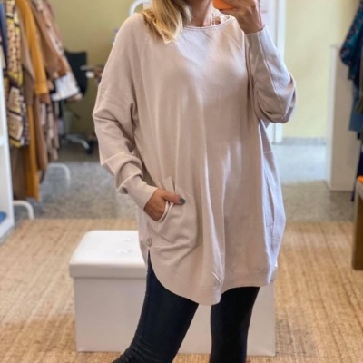 Túnica bege clara de manga comprida com bolso frontal, usada por mulher, em quarto com tapete e móveis