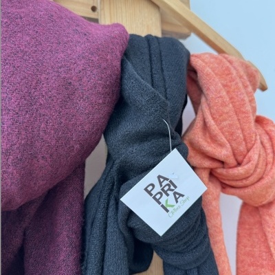 Três cachecóis coloridos pendurados em cabide de madeira com etiqueta