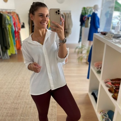 Mulher a tirar selfie numa loja de roupa, vestindo blusa branca e legging borgonha.
