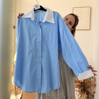 Camisa azul clara com gola e punhos brancos pendurada em cabide preto