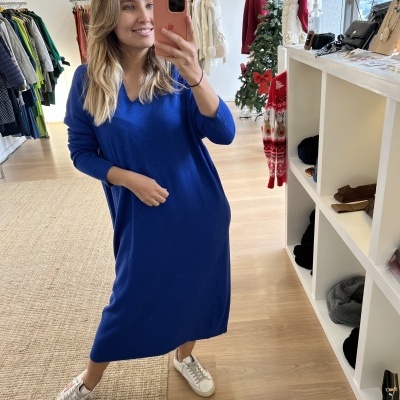 Mulher com vestido azul e sapatilhas numa loja de roupa com decoração de Natal.