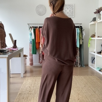 Pessoa de costas com conjunto castanho em loja de roupas com chão de madeira e tapete bege