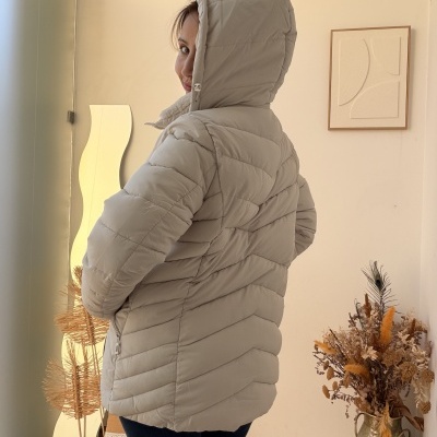 Casaco acolchoado cinza claro com capuz visto de trás com parede, quadro e vaso ao lado