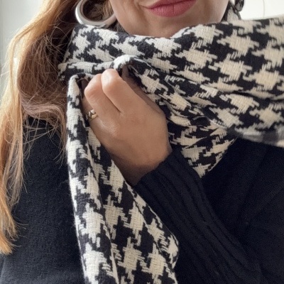 Pessoa com cachecol pied-de-poule preto e branco, blusa preta e brincos de argola prateados