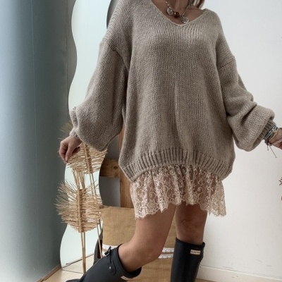 Mulher com roupa casual elegante composta por camisola cinza oversized, saia de renda creme e botas pretas Hunter.