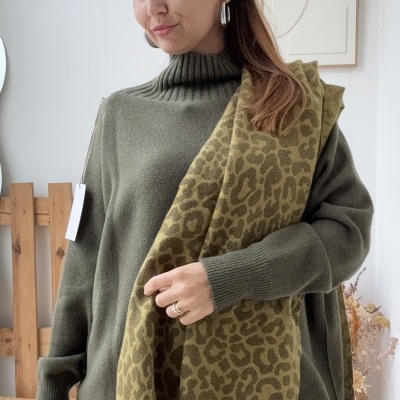 Mulher com gola alta verde e cachecol animal print em ambiente decorado minimalista