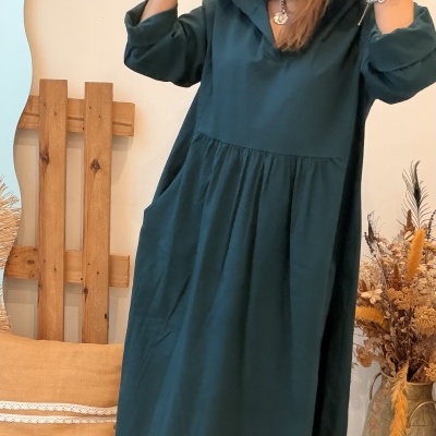 Vestido verde-escuro com capuz e botas castanhas em ambiente interior.