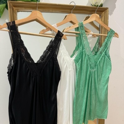 Três tops com alças largas e renda em preto, branco e verde claro em cabides de madeira