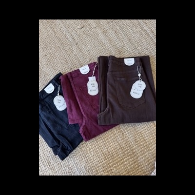 Três calças dobradas em preto, vermelho e castanho sobre tecido bege