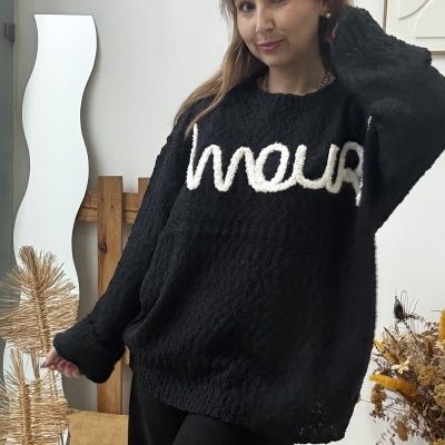 Mulher a usar camisola preta com letras brancas e calças pretas em ambiente interior decorado