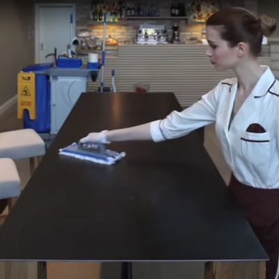 Mulher a limpar mesa preta numa sala com cadeiras e paredes de tijolo