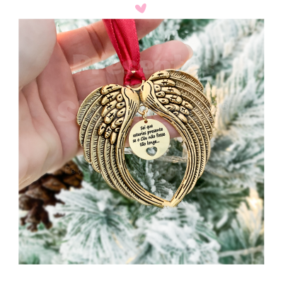 Ornamento natalício dourado em forma de asas com mensagem central e fita vermelha